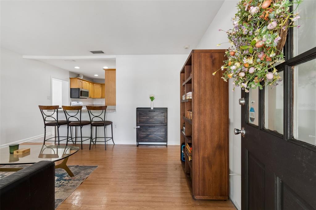 A living room features wood flooring, a bookshelf, a small cabinet, and a kitchen breakfast bar — 4602 W BAY VILLA AVENUE, TAMPA, FL