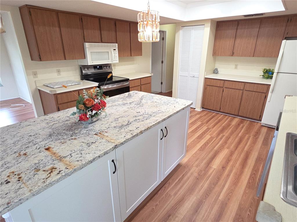 A kitchen features wood cabinets, a white island with a granite countertop, and wood flooring — 6264 DARIEN WAY, SPRING HILL, FL