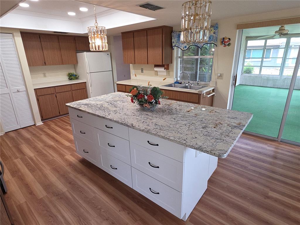 A kitchen features wood cabinets, a white island with granite countertops, and wood-look flooring — 6264 DARIEN WAY, SPRING HILL, FL