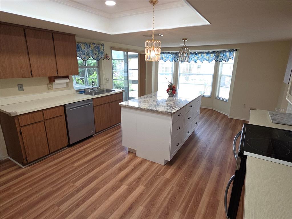 A kitchen features wood cabinets, a white center island with granite, and wood-look flooring — 6264 DARIEN WAY, SPRING HILL, FL