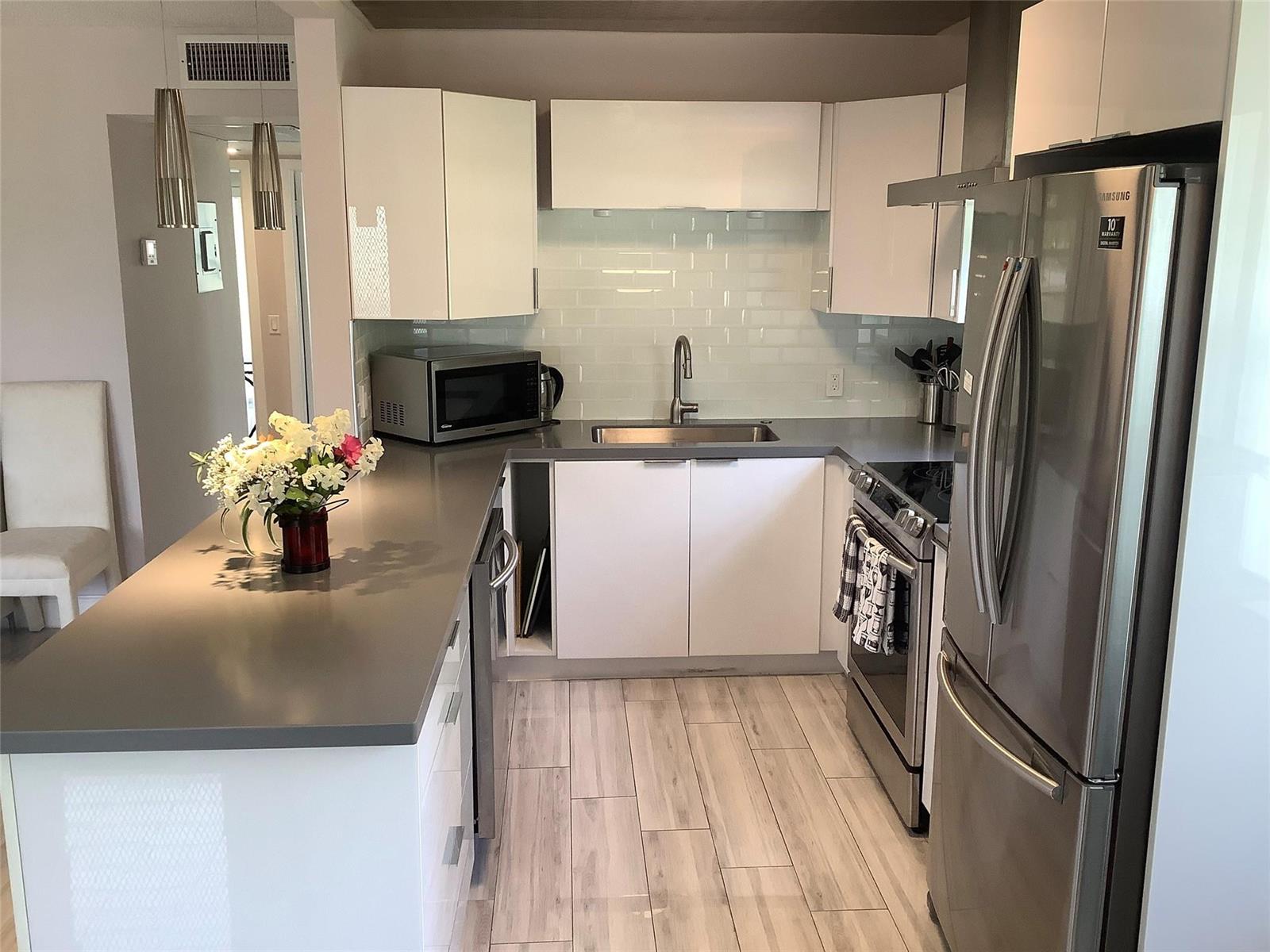 A modern kitchen features white cabinets, gray countertops, stainless steel appliances, and light wood-look flooring — 364 Dorset I # 364, Boca Raton FL 33434, BOCA RATON, FL