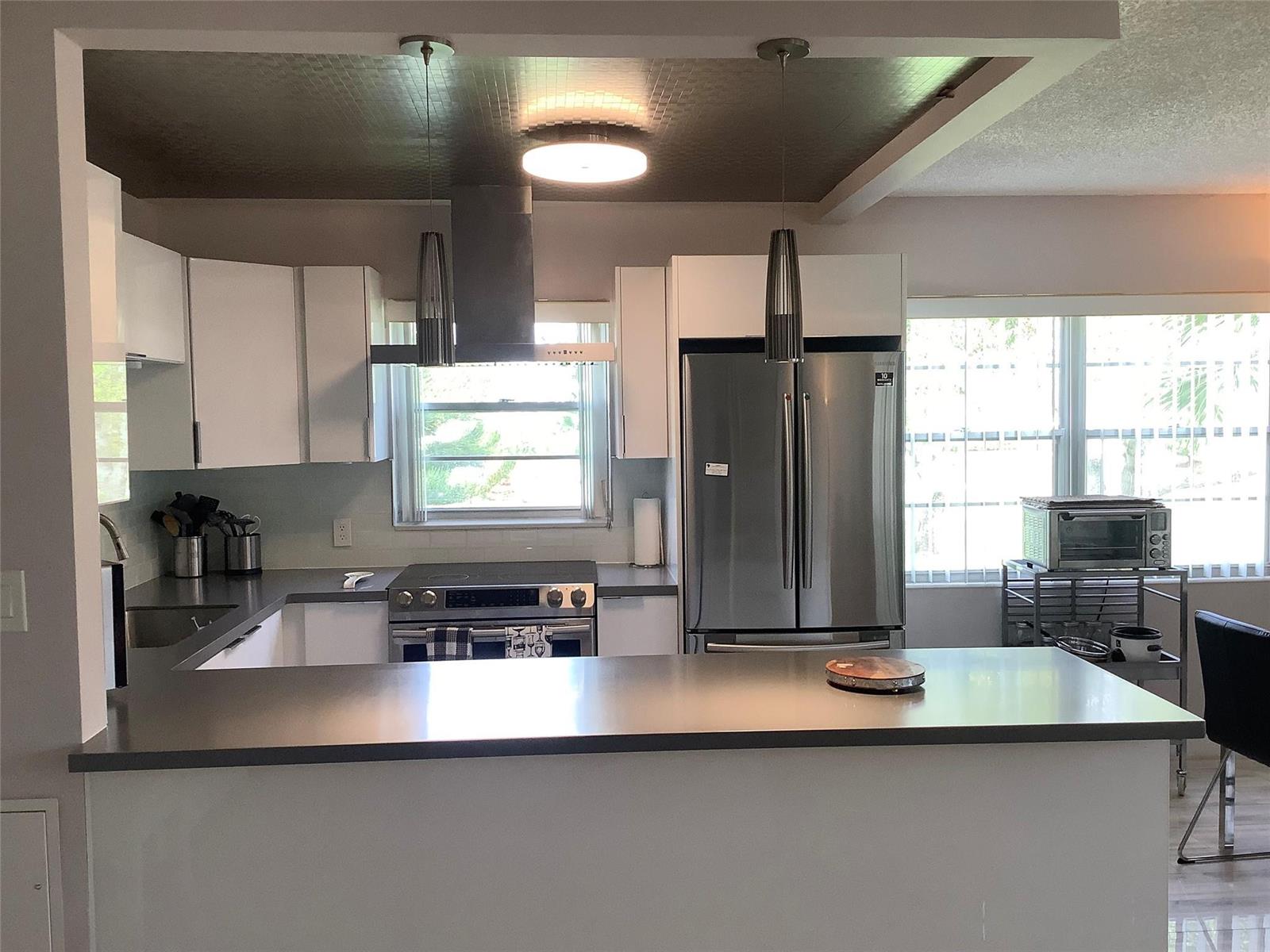 A modern kitchen features white cabinets, stainless steel appliances, and a gray countertop peninsula — 364 Dorset I # 364, Boca Raton FL 33434, BOCA RATON, FL