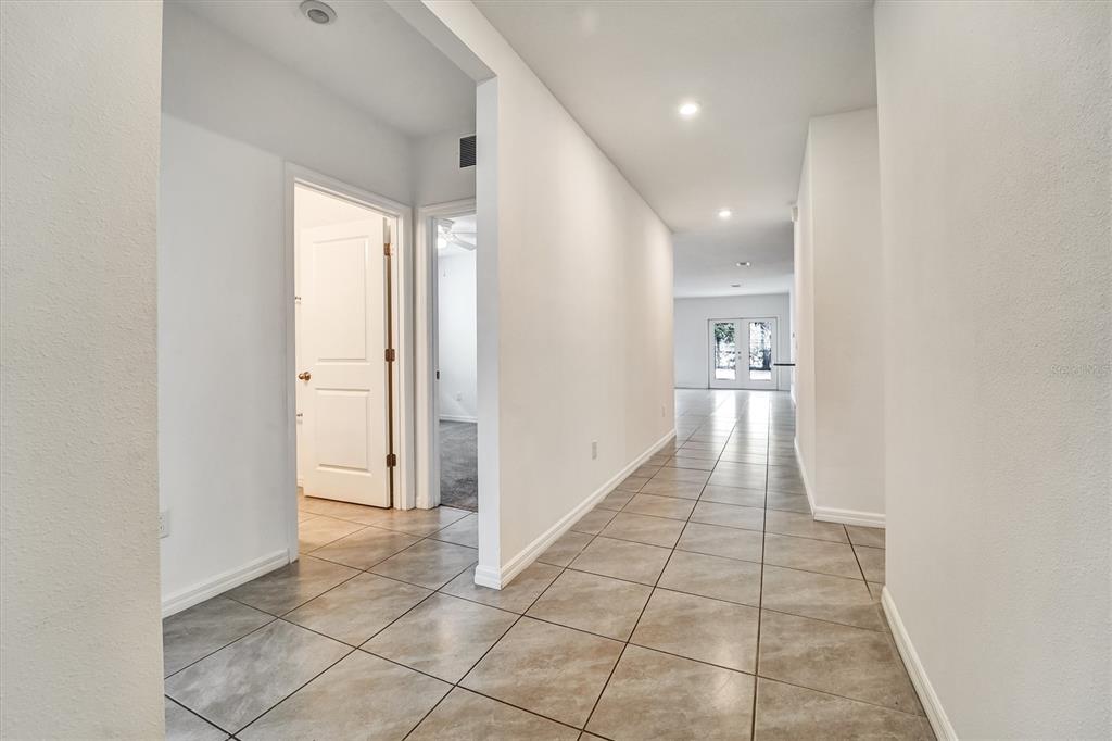 A tiled hallway leads to a doorway with double glass doors in the distance — 6963 SHELBY LYNN WAY, ZEPHYRHILLS, FL