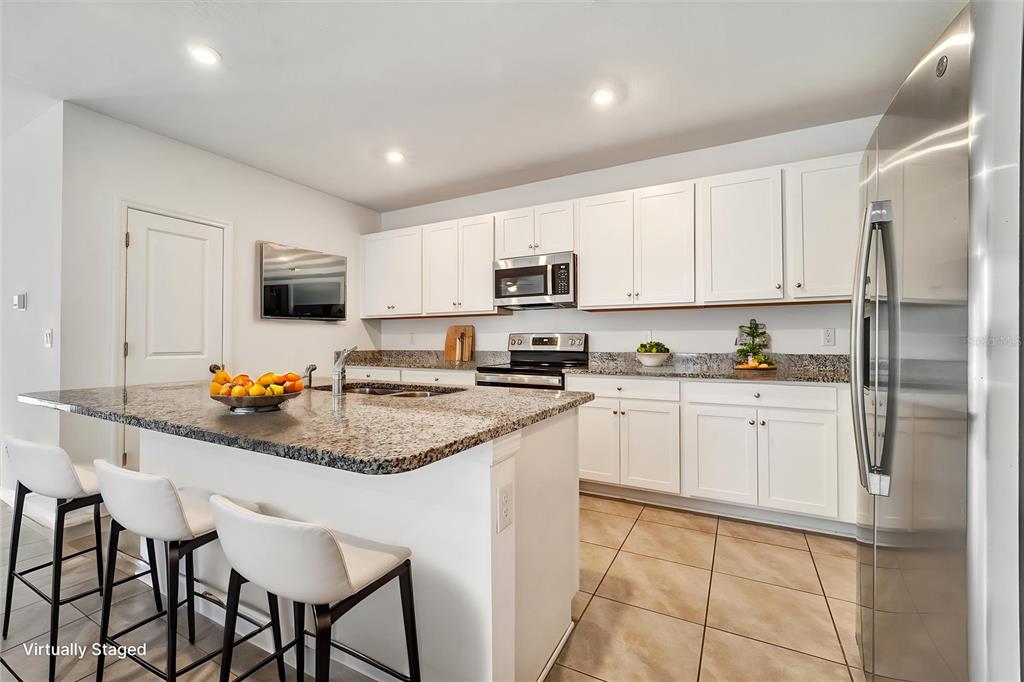 A kitchen features white cabinets, granite countertops, a center island with seating, and stainless appliances — 6963 SHELBY LYNN WAY, ZEPHYRHILLS, FL
