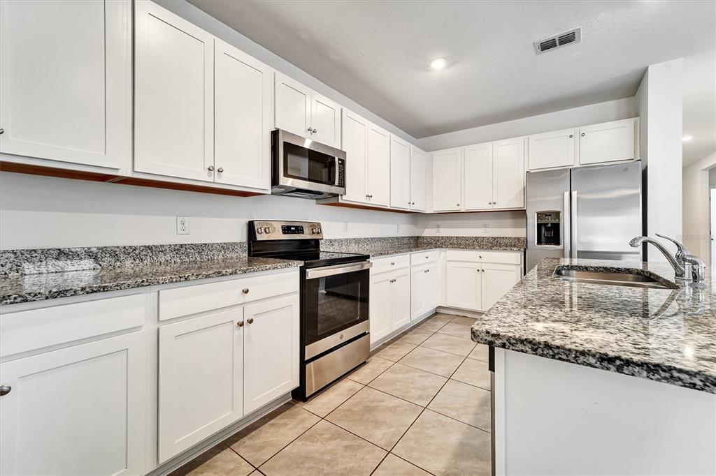 A kitchen features white cabinets, granite countertops, stainless steel appliances, and tile flooring — 6963 SHELBY LYNN WAY, ZEPHYRHILLS, FL
