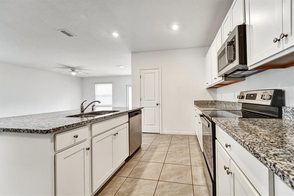 A kitchen features white cabinets, granite countertops, stainless steel appliances, and tile flooring — 6963 SHELBY LYNN WAY, ZEPHYRHILLS, FL