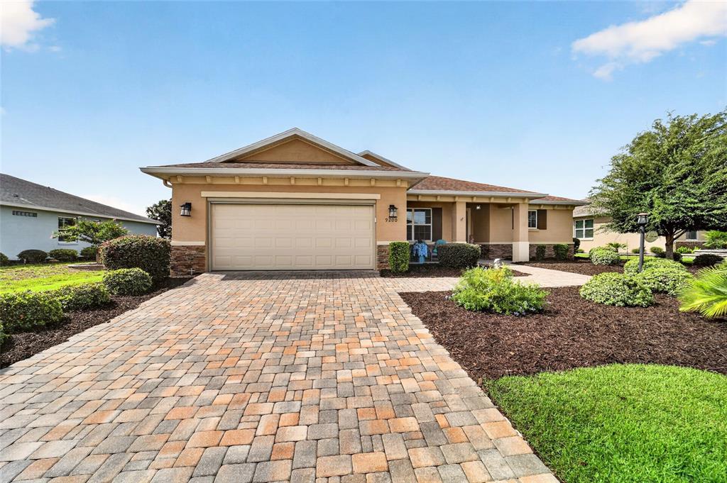 A single-story house with a tan stucco exterior, a paver driveway, and a two-car garage — 9200 SW 85TH PLACE, OCALA, FL