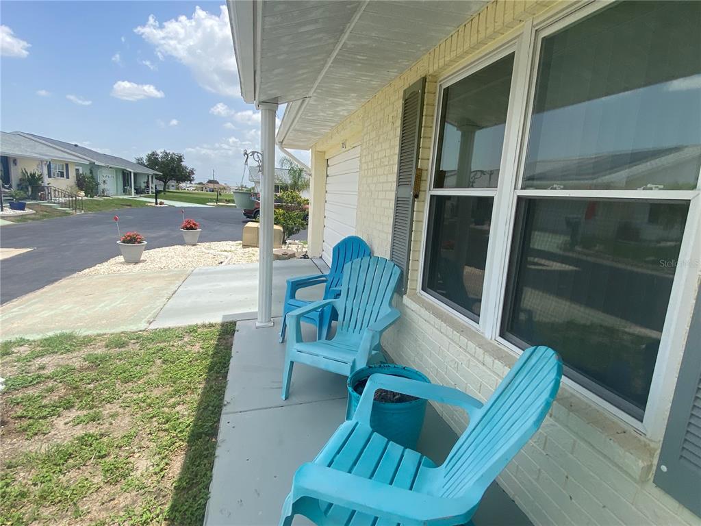 A covered concrete porch features three bright blue Adirondack chairs and a matching blue planter — 703 HUXLEY PLACE, SUN CITY CENTER, FL