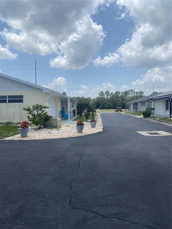 A paved street leads past a light-colored house with potted flowers and a gravel yard — 703 HUXLEY PLACE, SUN CITY CENTER, FL