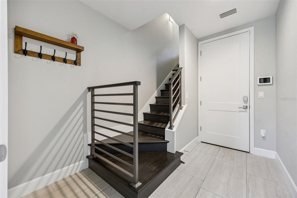 A modern entryway features a wooden coat rack, dark wood stairs, and a white door — 484 W PLANT STREET, WINTER GARDEN, FL