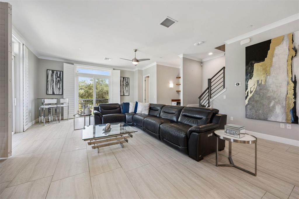 A modern living room features a large black leather sectional, glass coffee table, and tile flooring — 484 W PLANT STREET, WINTER GARDEN, FL
