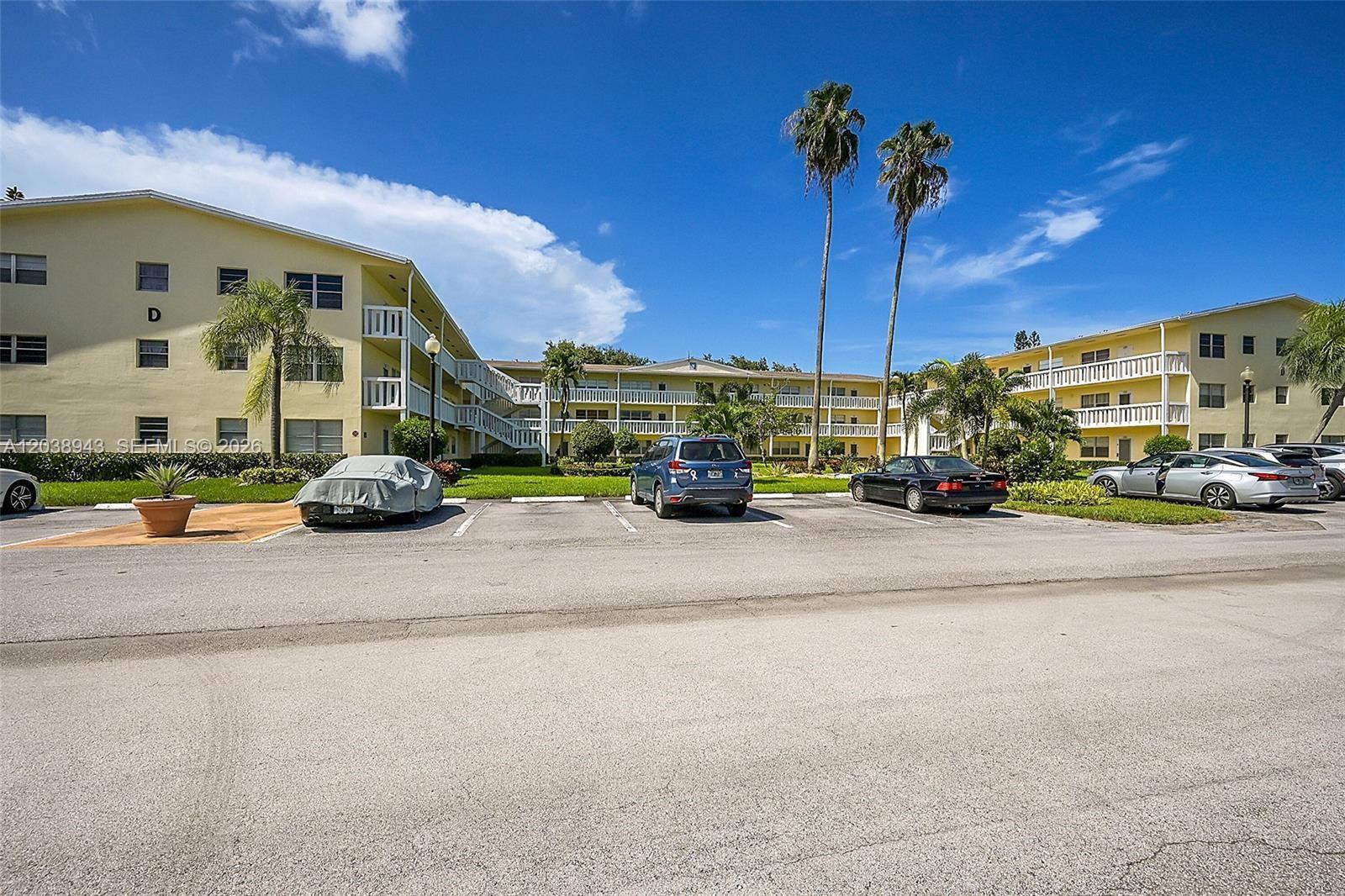 A multi-story yellow apartment building with a parking lot in the foreground — 82 Dorset B # B, Boca Raton FL 33434, BOCA RATON, FL