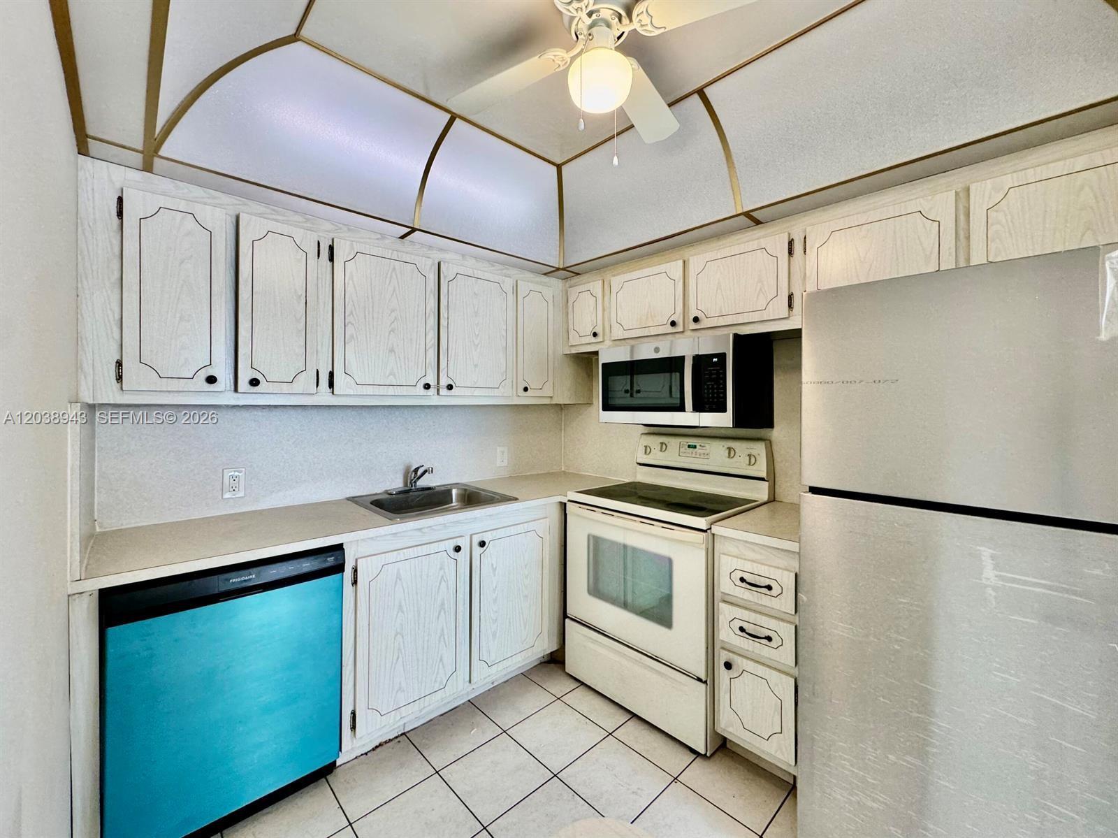A kitchen features white wood-grain cabinets, a blue dishwasher, white appliances, and a ceiling fan — 82 Dorset B # B, Boca Raton FL 33434, BOCA RATON, FL