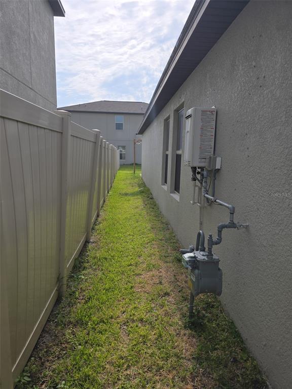 A side yard features a tan vinyl fence, a gas meter, and a tankless water heater — 5104 DANDELION STREET, APOLLO BEACH, FL
