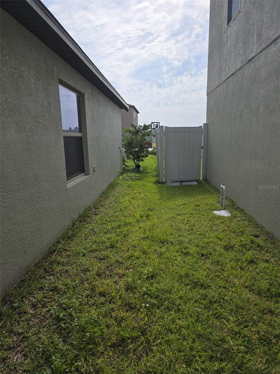A narrow grassy side yard sits between two stucco houses with a white privacy gate — 5104 DANDELION STREET, APOLLO BEACH, FL