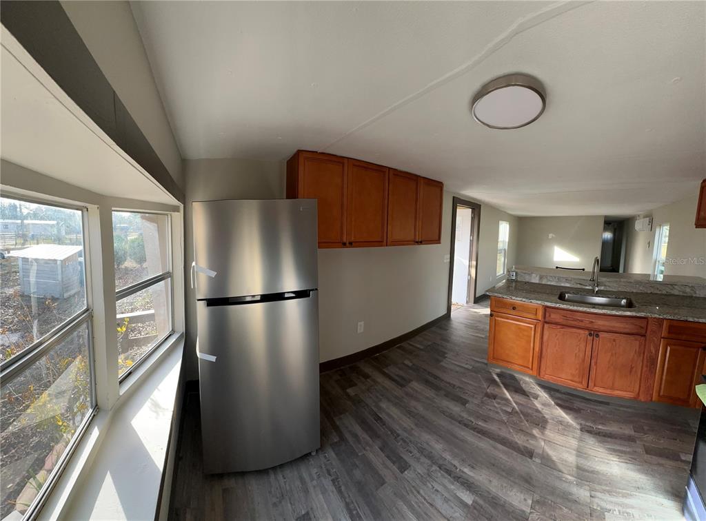 A kitchen features stainless steel appliances, wood cabinets, granite countertops, and wood-look flooring — 16083 NAPLES STREET, BROOKSVILLE, FL