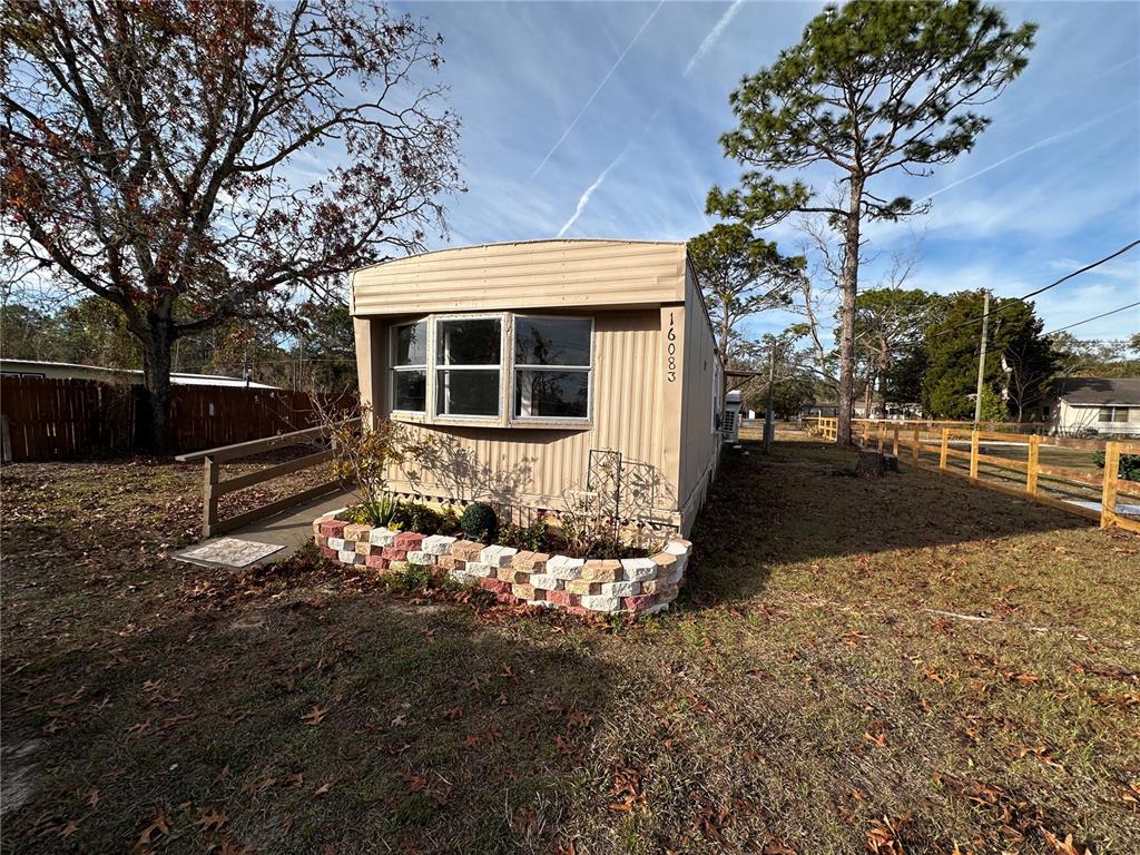 A tan mobile home features a bay window, a brick planter, and a wooden ramp — 16083 NAPLES STREET, BROOKSVILLE, FL