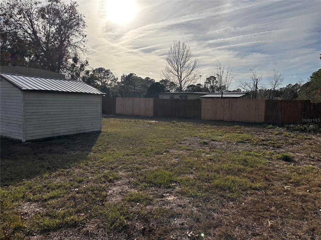 A backyard features a small shed, a wooden privacy fence, and sparse grass — 16083 NAPLES STREET, BROOKSVILLE, FL