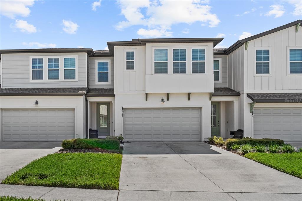 A two-story townhouse exterior features a two-car garage, light siding, and a concrete driveway — 1621 SANIBEL DRIVE, DAVENPORT, FL