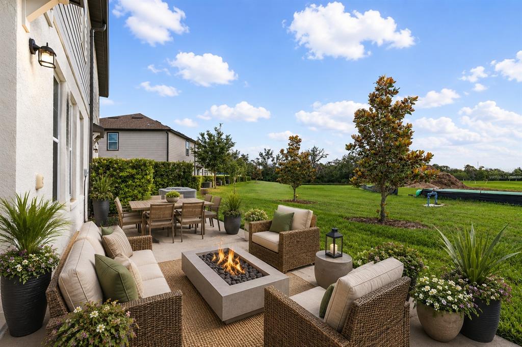 A patio features a fire pit, wicker furniture, and potted plants overlooking a grassy backyard — 1621 SANIBEL DRIVE, DAVENPORT, FL