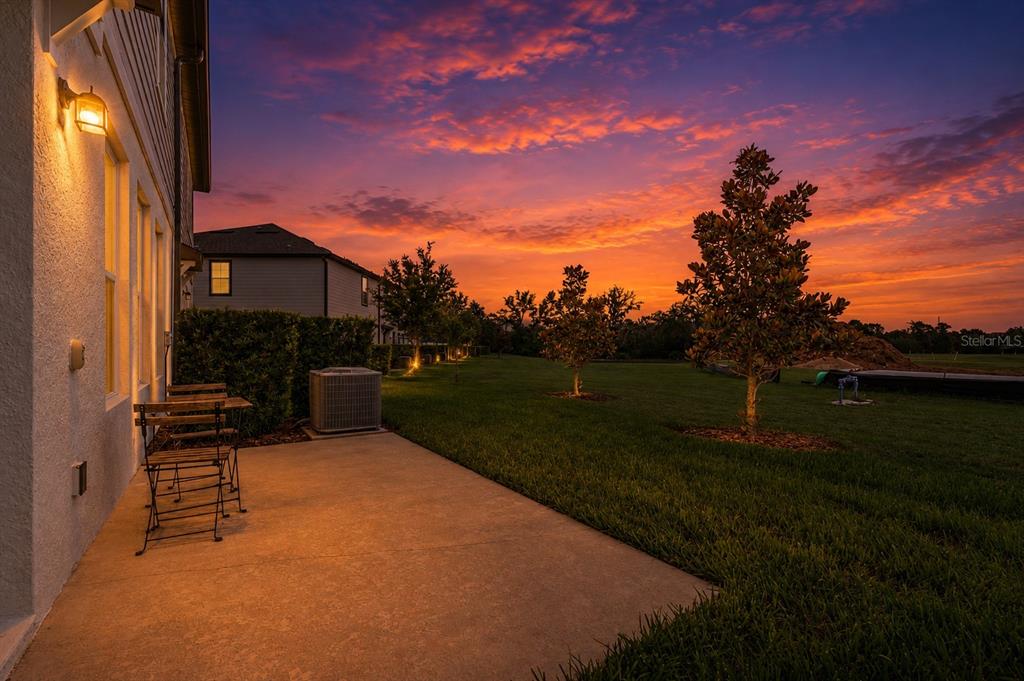 A concrete patio sits beside a house exterior at sunset with a view of trees — 1621 SANIBEL DRIVE, DAVENPORT, FL
