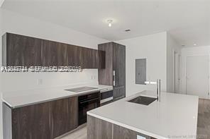 A modern kitchen features dark wood cabinetry, white countertops, and a central island with sink — 480 NE 31 ST # 2306, Miami FL 33137, MIAMI, FL