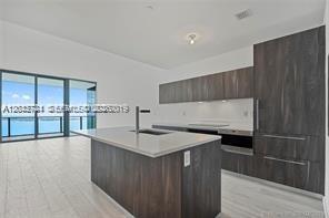 A modern kitchen features dark wood cabinetry, a central island, and floor-to-ceiling windows — 480 NE 31 ST # 2306, Miami FL 33137, MIAMI, FL