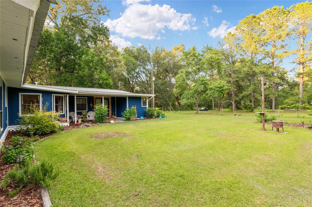 A blue house with a metal roof overlooks a large, grassy backyard with mature trees — 4912 NW 170TH STREET, ALACHUA, FL