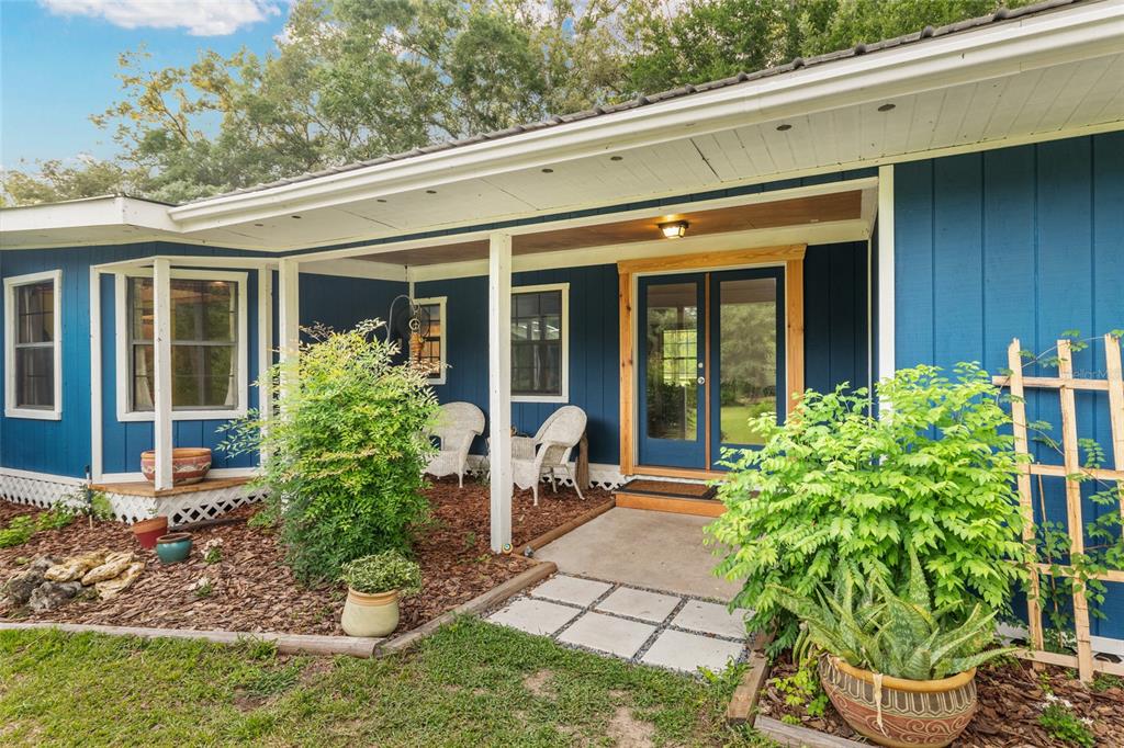 A blue house exterior features a covered porch, double glass doors, and a landscaped yard — 4912 NW 170TH STREET, ALACHUA, FL