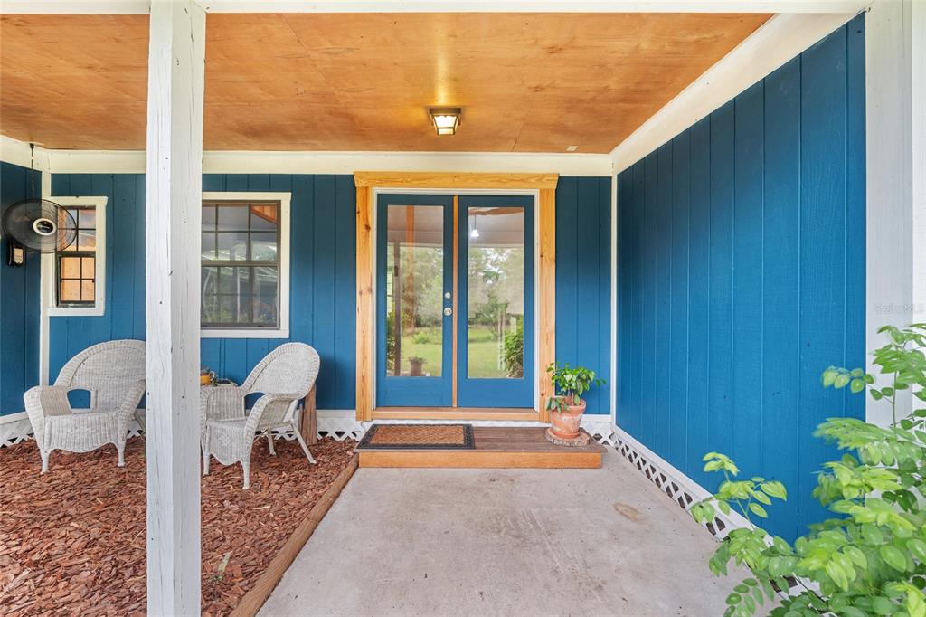 A covered porch with blue siding, two wicker chairs, and a double glass front door — 4912 NW 170TH STREET, ALACHUA, FL