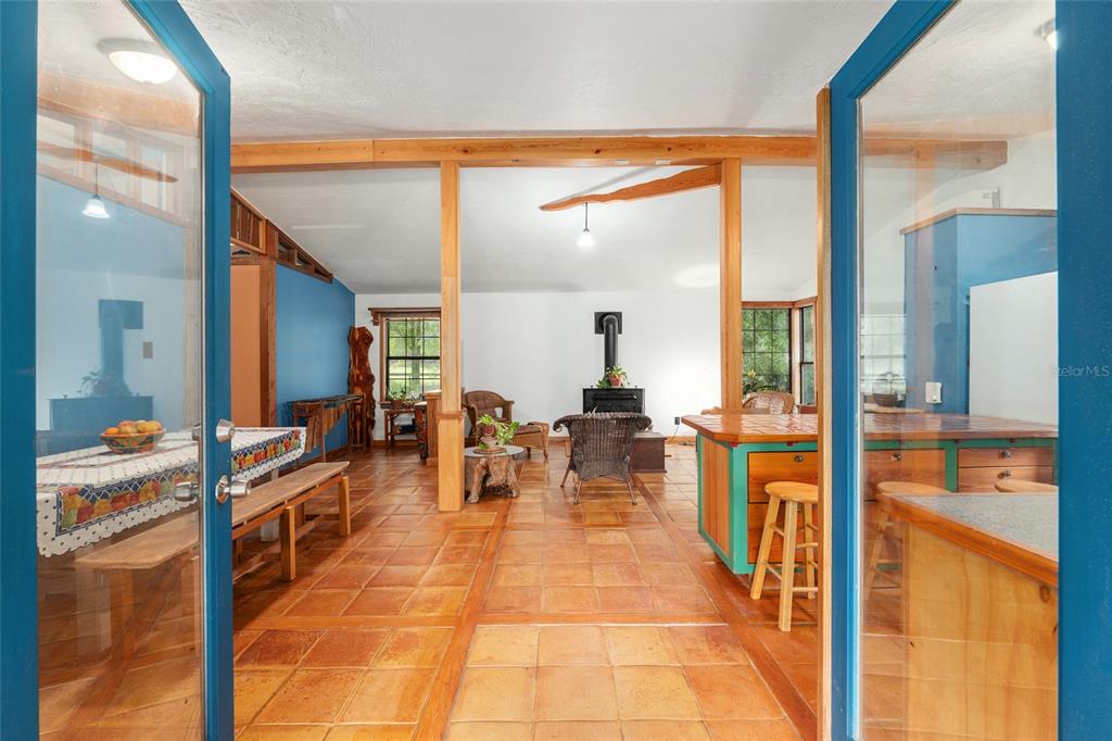 An open-concept living and dining area features terracotta tile floors, wood beams, and blue walls — 4912 NW 170TH STREET, ALACHUA, FL
