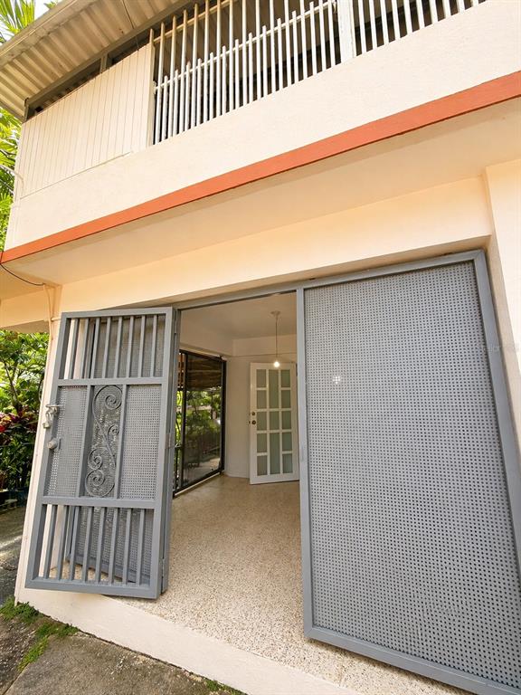 A ground-level entryway features gray metal security gates opening into a room with terrazzo flooring — R517 COLLORES WARD, JUANA DIAZ, PR