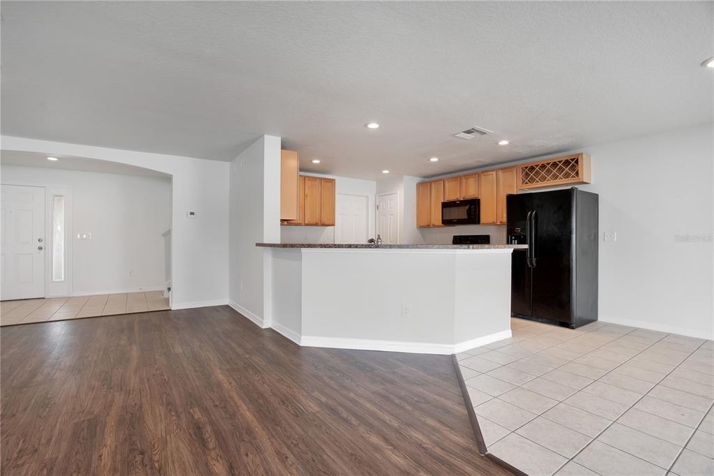 An open-concept kitchen features light wood cabinets, a black refrigerator, and a breakfast bar — 12012 CITRUS LEAF DRIVE, GIBSONTON, FL