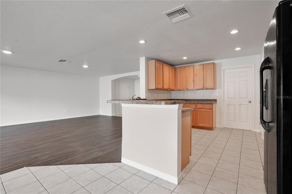 A kitchen with wood cabinets and tile flooring opens to a living area with flooring — 12012 CITRUS LEAF DRIVE, GIBSONTON, FL