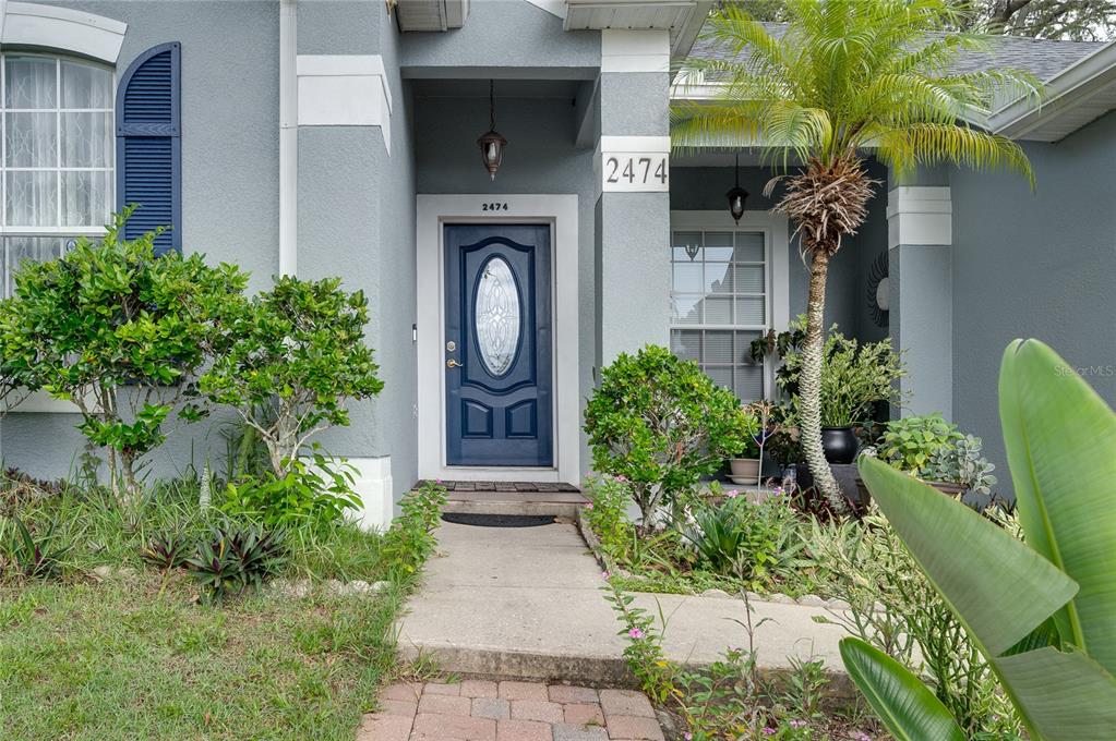 The exterior of a house features a blue front door, a palm tree, and landscaping — 2474 CIMMARON ASH WAY, APOPKA, FL