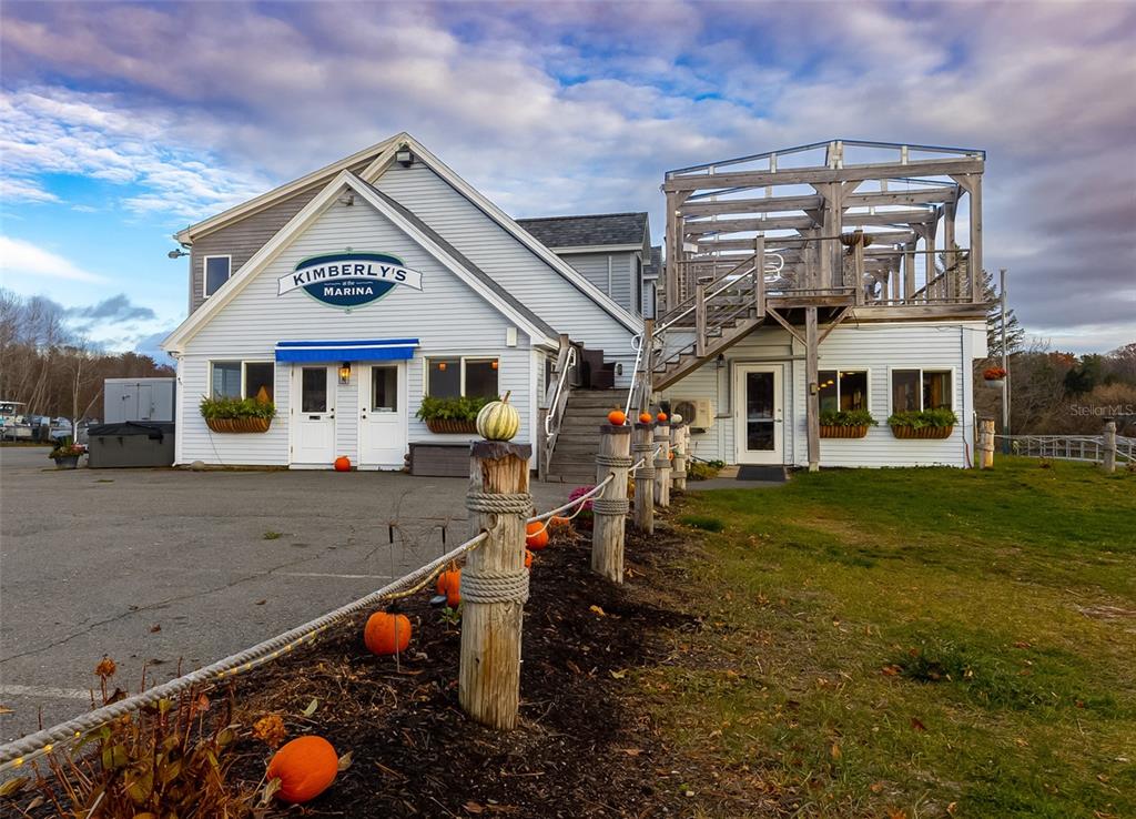 A two-story building with a marina sign and a wooden deck sits near a lawn — 108 MARINA ROAD, HAMPDEN, ME