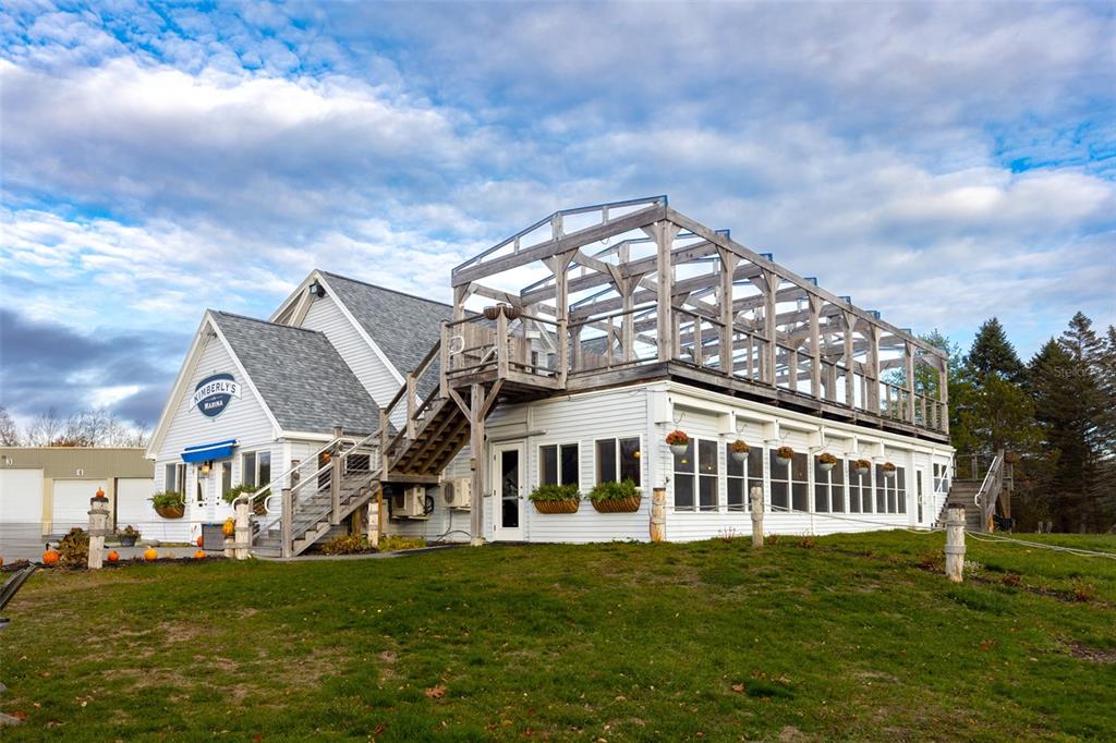A white building with a large wooden deck structure sits on a grassy lawn — 108 MARINA ROAD, HAMPDEN, ME