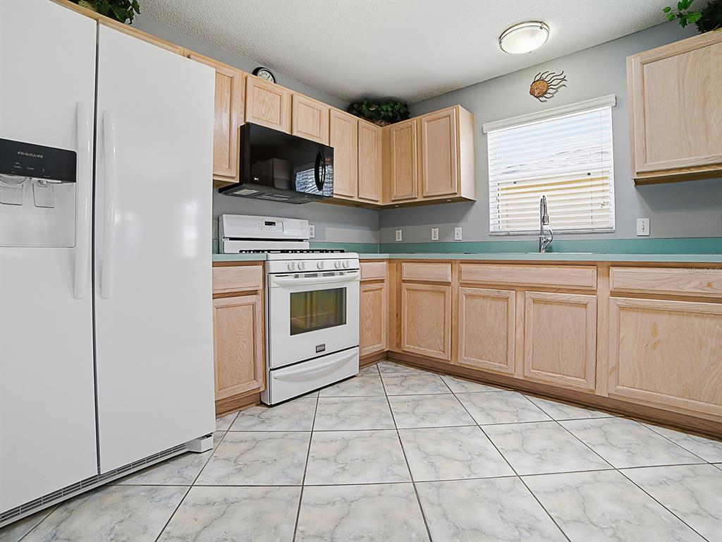 A kitchen features light wood cabinets, white appliances, a teal backsplash, and marble-patterned tile flooring — 872 WINCHESTER COURT, THE VILLAGES, FL