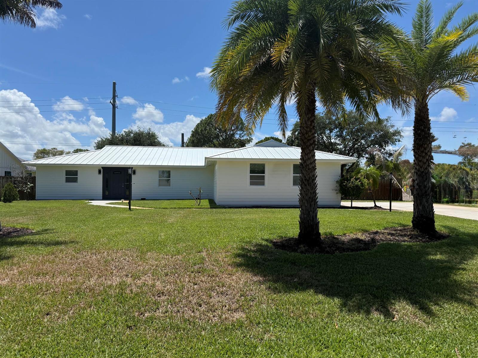 A white single-story house with a metal roof sits behind two palm trees — 5883 Set-n-sun Place, Jupiter FL 33458, JUPITER, FL