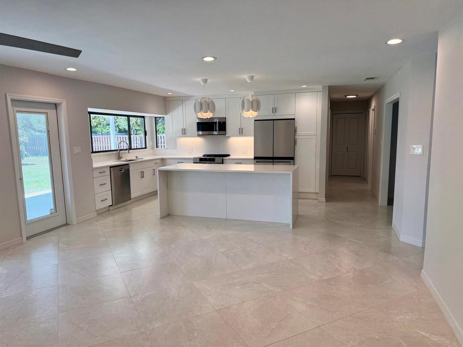 A modern kitchen features white cabinetry, a central island, stainless steel appliances, and tile flooring — 5883 Set-n-sun Place, Jupiter FL 33458, JUPITER, FL