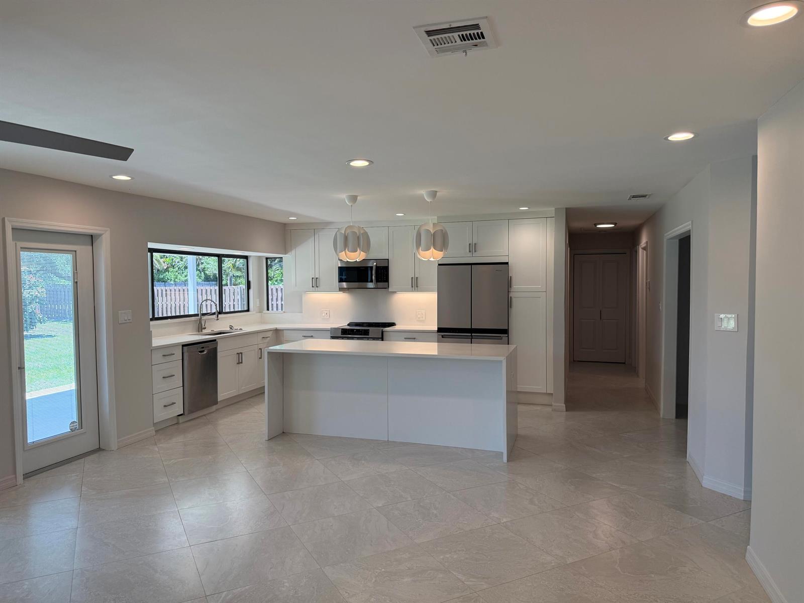 A modern kitchen features white cabinetry, a central island, stainless steel appliances, and tile flooring — 5883 Set-n-sun Place, Jupiter FL 33458, JUPITER, FL