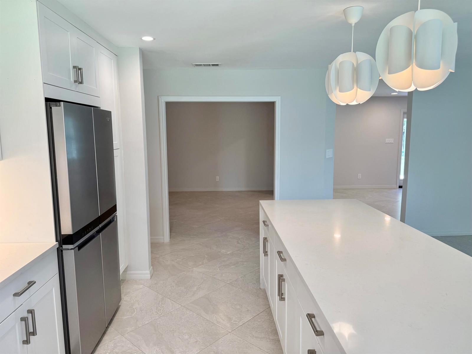 A modern kitchen features white cabinetry, a stainless steel refrigerator, and a large quartz island — 5883 Set-n-sun Place, Jupiter FL 33458, JUPITER, FL