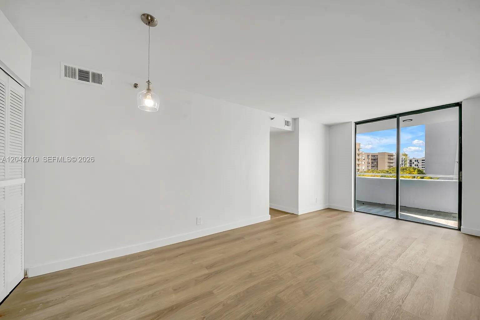 An empty room with light wood flooring, a single pendant light, and a sliding glass door — 501 SW 1st St # 502, Miami FL 33130, MIAMI, FL