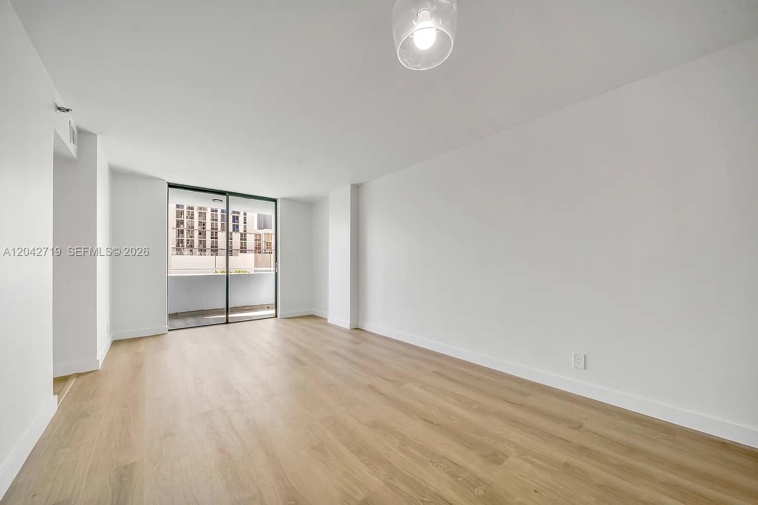 An empty room with light wood flooring, white walls, and a sliding glass balcony door — 501 SW 1st St # 502, Miami FL 33130, MIAMI, FL