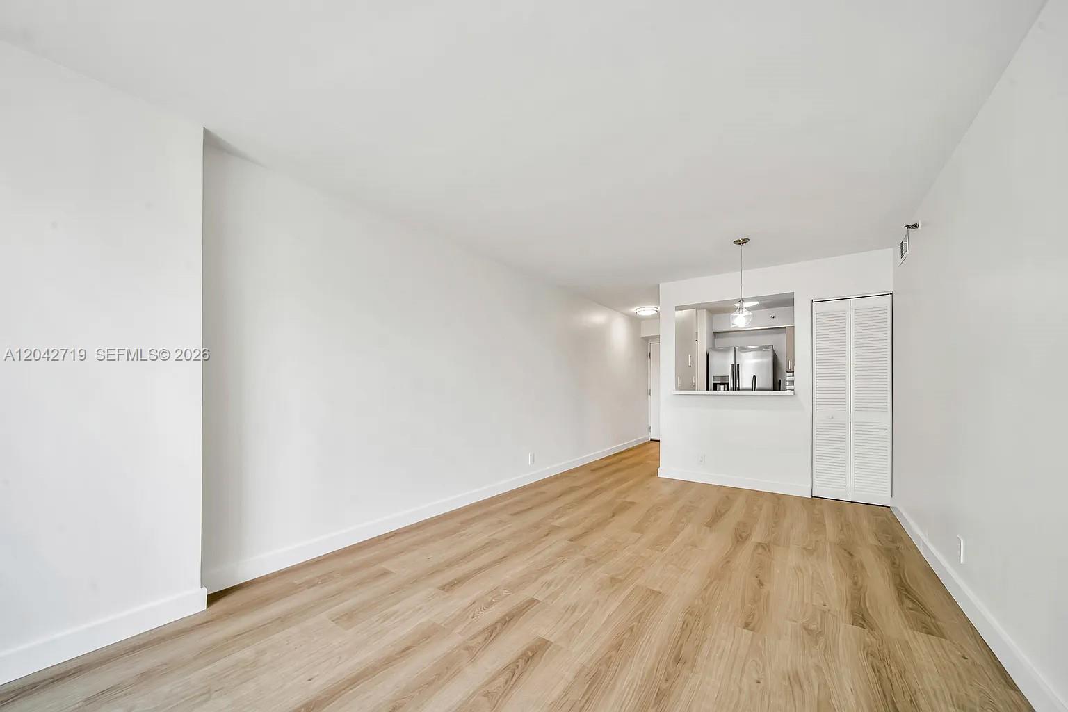 An empty living area features light wood-look flooring, white walls, and a pass-through kitchen — 501 SW 1st St # 502, Miami FL 33130, MIAMI, FL