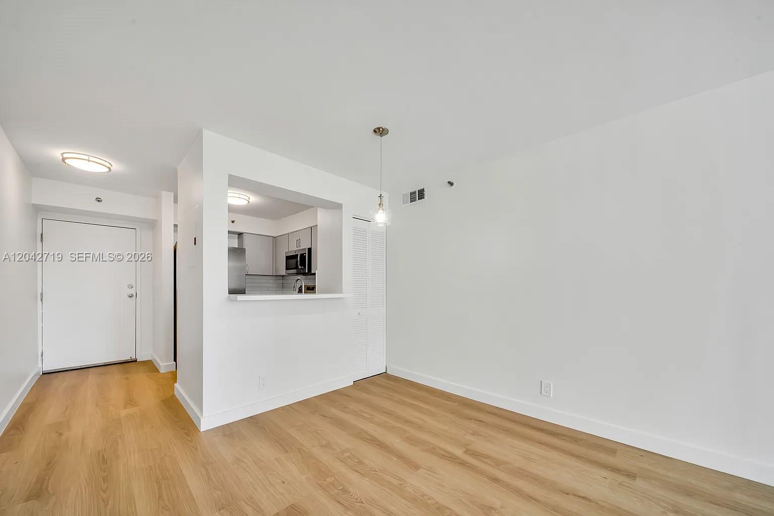 An empty room features light wood-look flooring, white walls, and a pass-through kitchen window — 501 SW 1st St # 502, Miami FL 33130, MIAMI, FL