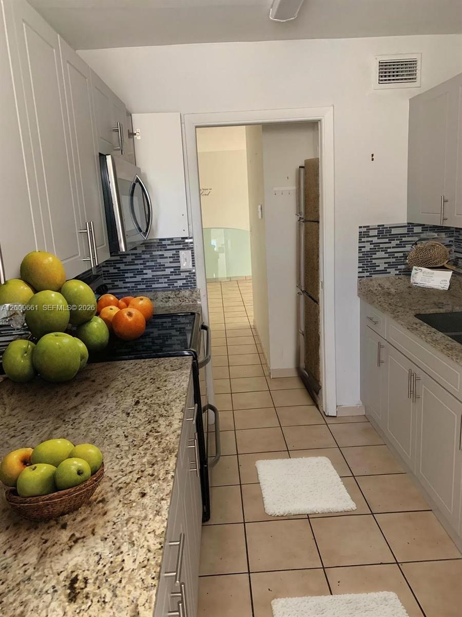 A galley kitchen features light gray cabinets, granite countertops, and a blue tiled backsplash — 7345 W 4th Ave # 203, Hialeah FL 33014, HIALEAH, FL