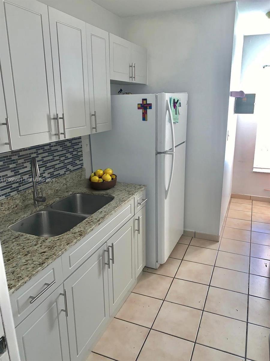 A kitchen features white cabinets, granite countertops, a double-basin sink, and a white refrigerator — 7345 W 4th Ave # 203, Hialeah FL 33014, HIALEAH, FL