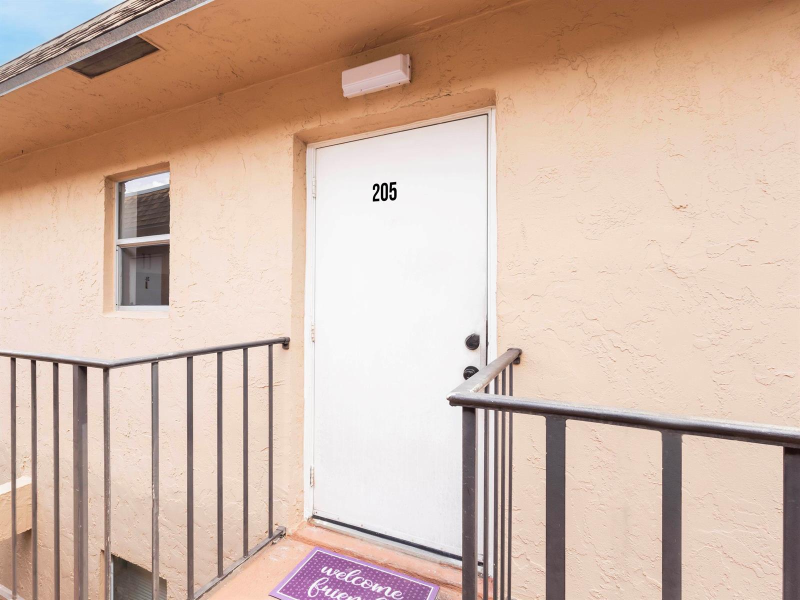 A white door labeled 205 is set in a tan exterior wall with a metal railing — 450 SW 2nd Avenue # 2050, Boca Raton FL 33432, BOCA RATON, FL