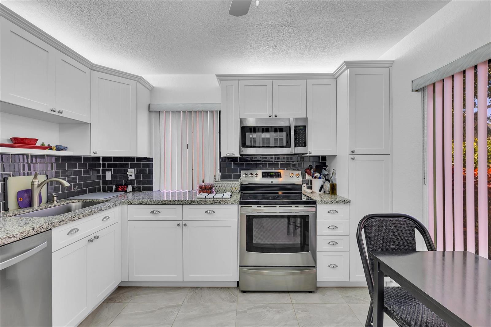 A kitchen features white cabinets, stainless steel appliances, granite countertops, and a dark tile backsplash — 2260 Seagrape Circle, Coconut Creek FL 33066, COCONUT CREEK, FL